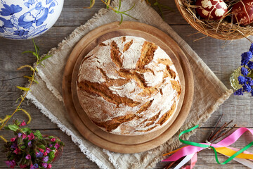 Sourdough bread with spring flowers and Easter eggs on a wooden table, top view