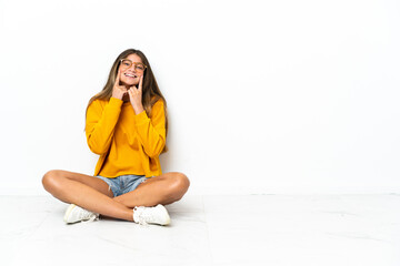 Young woman sitting on the floor isolated on white background smiling with a happy and pleasant...