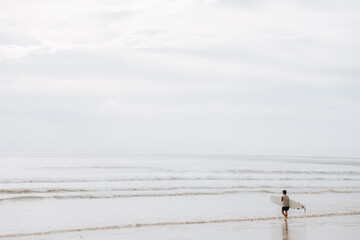 Asian male surfer going for surfing in the sea. Man carrying surfboard walking in to the sea for...