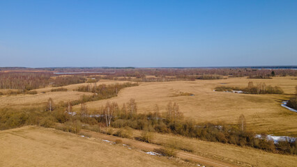 Fototapeta na wymiar Aerial view of fields with copse, dry yellow grass, a stream, remnants of snow in early spring. Nature background.