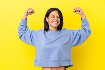 Young caucasian woman isolated on yellow background doing strong gesture - obrazy, fototapety, plakaty