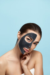 Beauty Woman Face Skin Care Mask. Portrait of a Beautiful Female with a Black Mask of Clay on Face .  Spa treatment . Girl Model with Moisturizer Cosmetic Mask Touches her Face.