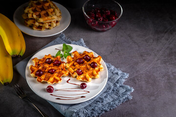 Belgian or Brussels waffles with frozen cherries. Homemade cottage cheese banana waffle in a plate on a dark table. Copy space
