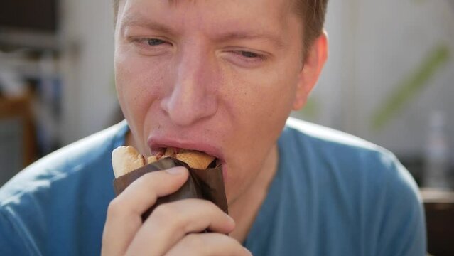 portrait of young man in blue shirt eating not tasty shawarma kebab. The man  mouth-watering fast food in the street