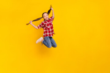 Photo of charming excited schoolgirl wear checkered shirt jumping high arms ponytails empty space...