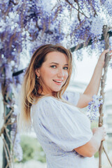 Pretty young woman is standing next to wisteria. Girl enjoying spring time. Spring outfit. 