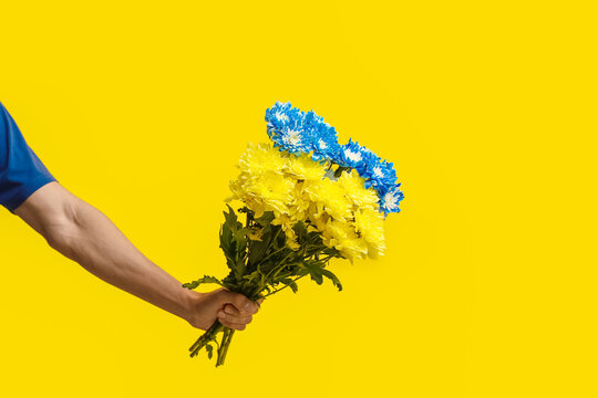 Male hand holding bouquet of flowers painted in colors of Ukrainian flag on yellow background