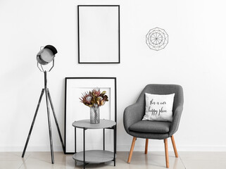 Stylish interior with modern armchair, blank picture frames, table and lamp