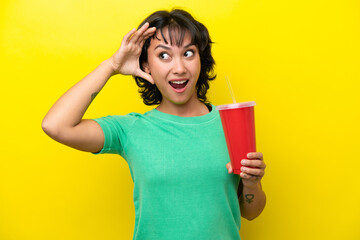Young Argentinian woman holding a soda isolated on yellow background doing surprise gesture while looking to the side