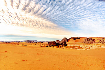 Fototapeta na wymiar Sahara desert of Tadrart Rouge. Colorful sand, Rocky Mountains, sky with sunlight diffusing in stratus clouds.