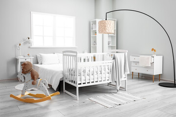 Interior of stylish bedroom with bed, crib and toy bear on rocking horse