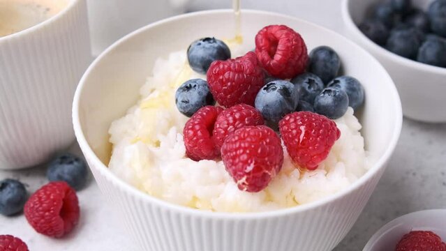 Pouring syrup rice pudding with berries and butter. Porridge bowl with raspberries and blueberries.