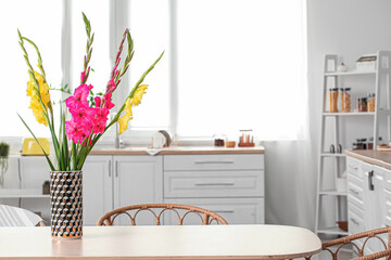Vase with beautiful gladiolus flowers on table in kitchen