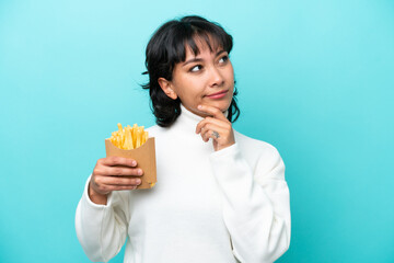Young Argentinian woman holding fried chips isolated on blue background having doubts while looking up