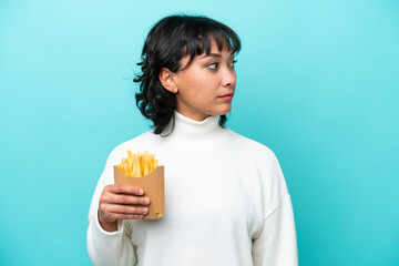Young Argentinian woman holding fried chips isolated on blue background looking to the side