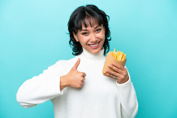 Young Argentinian woman holding fried chips isolated on blue background giving a thumbs up gesture