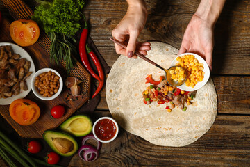 Woman preparing tasty burrito with meat on wooden background