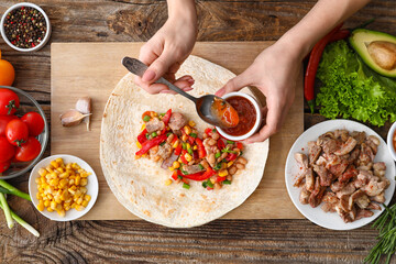 Woman preparing tasty burrito with meat on wooden background - obrazy, fototapety, plakaty