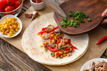 Preparing of tasty burrito with meat on wooden background