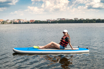 pretty slim woman floats on sup board and long paddle on city lake