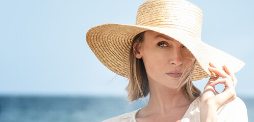 Beauty portrait of beautiful blonde caucasian girl in summer straw hat posing at the beach. Vacation vibe. Sunny day. Travel, tourism concept.