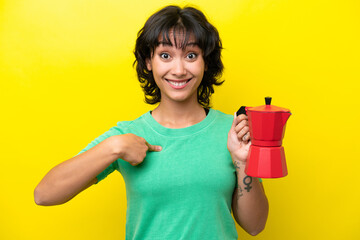 Young Argentinian woman holding coffee pot isolated on yellow background with surprise facial expression