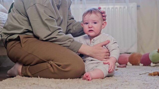 The mother pities the crying baby and strokes his head with her hand, age eight months