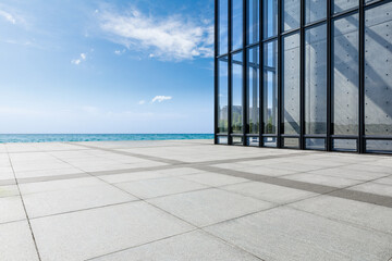 Empty square floor and glass wall building with lake under blue sky