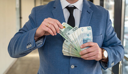 a handsome promising man in a suit and tie holds a large sum of Polish zlotys.