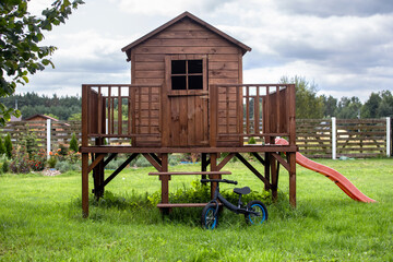 Fototapeta na wymiar Garden and wooden house for children. Toy bike slide