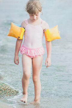 Sad adorable girl in pink swimsuite going on sea beach.