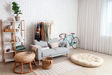 Sofa, shelf unit and rack with sweaters near white brick wall in living room interior