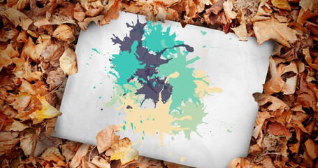 Image of multiple colorful stains over white paper and leaves