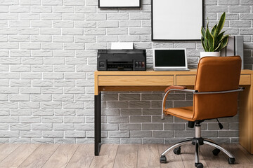Comfortable workplace with modern laptop and printer near grey brick wall