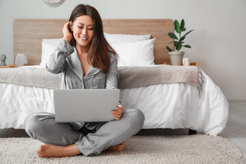 Young Asian barefoot woman using laptop in bedroom