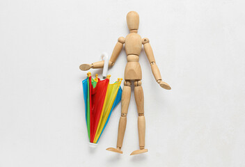 Wooden mannequin with umbrella on light background
