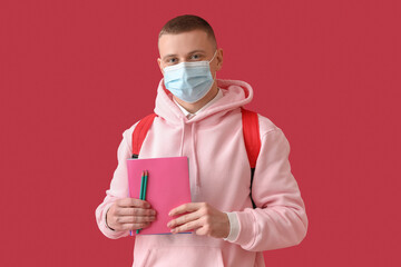 Male student in medical mask with copybooks on red background