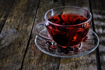 Cup karkade tea with bright red shade wooden background.