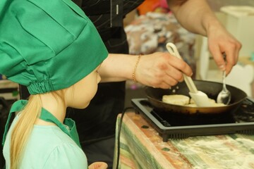 A little girl of 5 years old is learning to cook cheesecakes. In a green hat and apron.