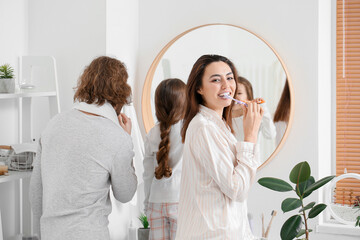 Young woman with her husband and little daughter brushing teeth in bathroom
