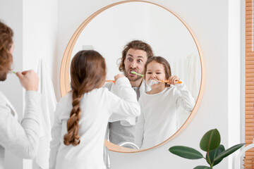 Little girl with her father brushing teeth near mirror in bathroom