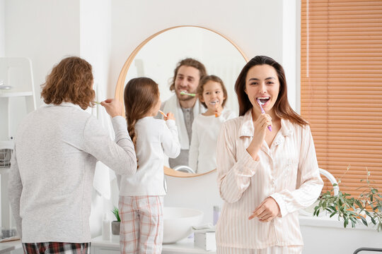 Young woman with her husband and little daughter brushing teeth in bathroom