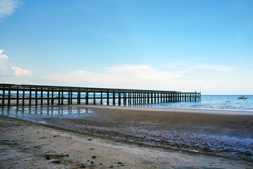 Concrete jetty that extends from the coast to the sea with beautiful sandy beach and blue sky background.