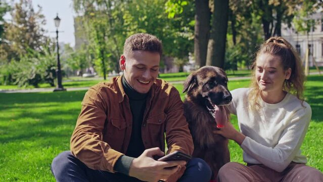 Young couple sitting on lawn with lovely german shepherd dog, taking a selfie