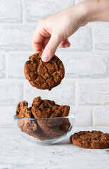A woman's hand takes an oatmeal cookie with chocolate chips on a light background. Breakfast concept.