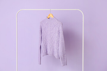 Rack with lilac sweater on color background