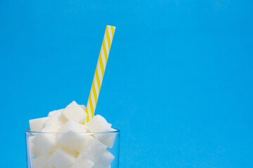 Glass with refined sugar cubes and a drinking tube on a blue background.