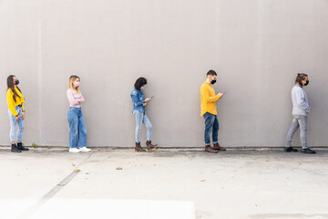 Obraz premium Group of friends at a safe distance with protective face masks against Coronavirus infections, Covid-19 - Outdoor safety concept before entering a store during the pandemic - People using smartphone