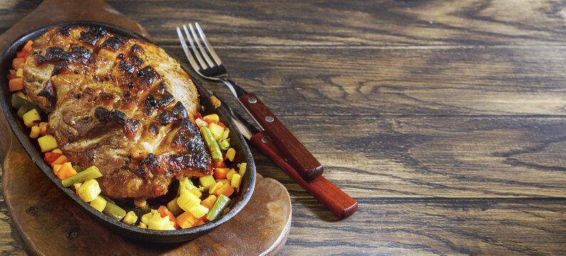 Home made roasted pork in frying pan with sliced vegetables on oak wooden background with copy space