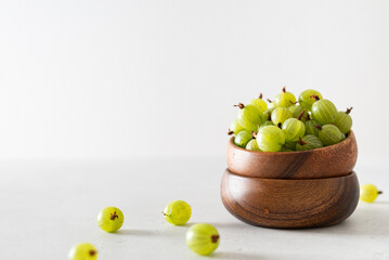 Ripe green gooseberries in a wooden bowl on a white background. Harvest concept. Vegetarian food. Side view, copy space. Gardening
